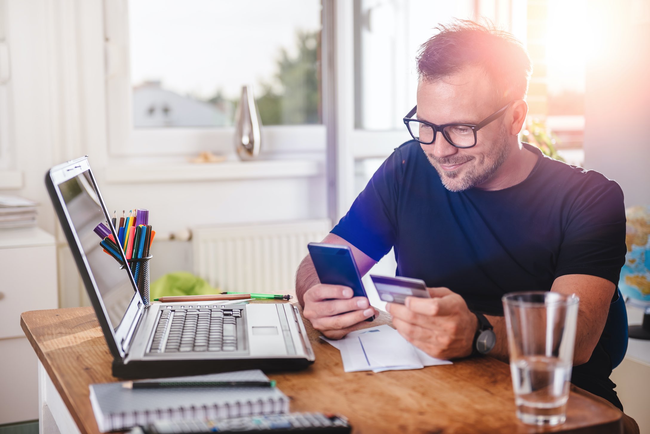 man working at a laptop, holding a phone and a credit card